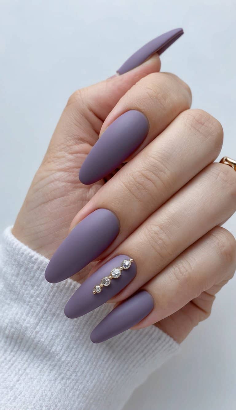 Side view of long almond matte wedding nails painted smoky lavender, with a horizontal row of rhinestones decorating one nail against a pale background.