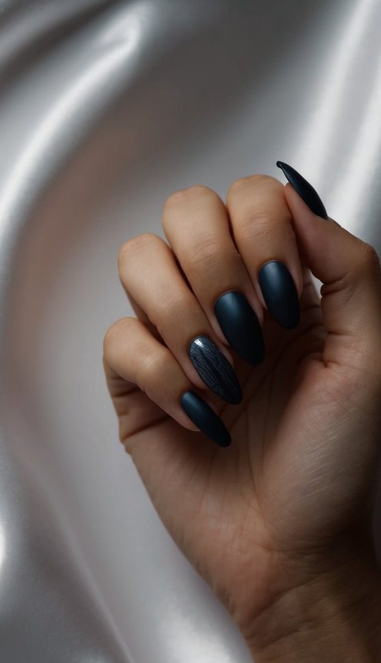 A hand with matte midnight navy almond-shaped nails, featuring a single accent nail with a subtle vertical shimmer overlay for a refined, understated wedding manicure.