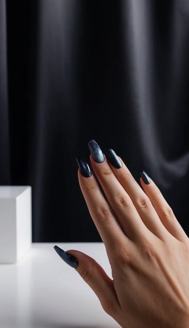 A dimly lit room with a black satin backdrop, showcasing a set of dark and moody nail designs on a sleek, minimalist surface