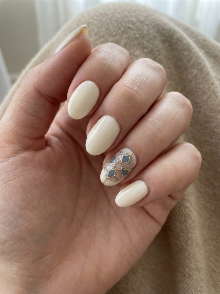 Manicured fingers gently curled, displaying short wedding nails painted glossy off-white, alongside a detailed accent nail with gold-lined geometric petal shapes in muted blue and pink.