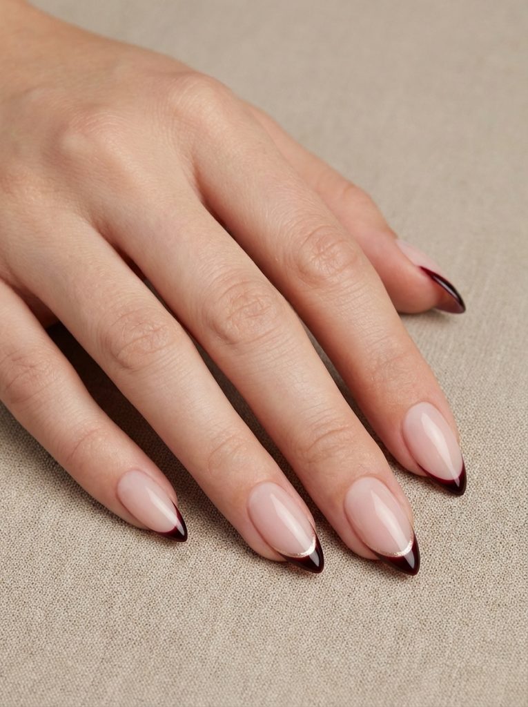 Close-up of a manicured hand featuring short wedding nails in glossy nude-pink polish with pointed burgundy French tips.