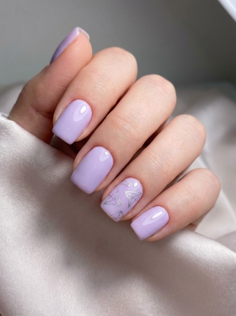 Fingers gently curled against silky fabric display short square wedding nails painted in soft violet, featuring one accent nail detailed with thin metallic triangle line art.