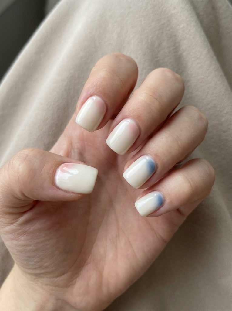 Fingers gently curved inward display short square wedding nails painted in milky ivory, accented by subtle steel-blue gradient detailing on two nails.