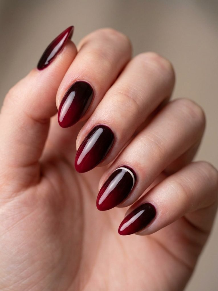 Close-up of a hand displaying ombre wedding nails in a deep black cherry fading into rich ruby red, shaped in glossy almonds against a neutral background.