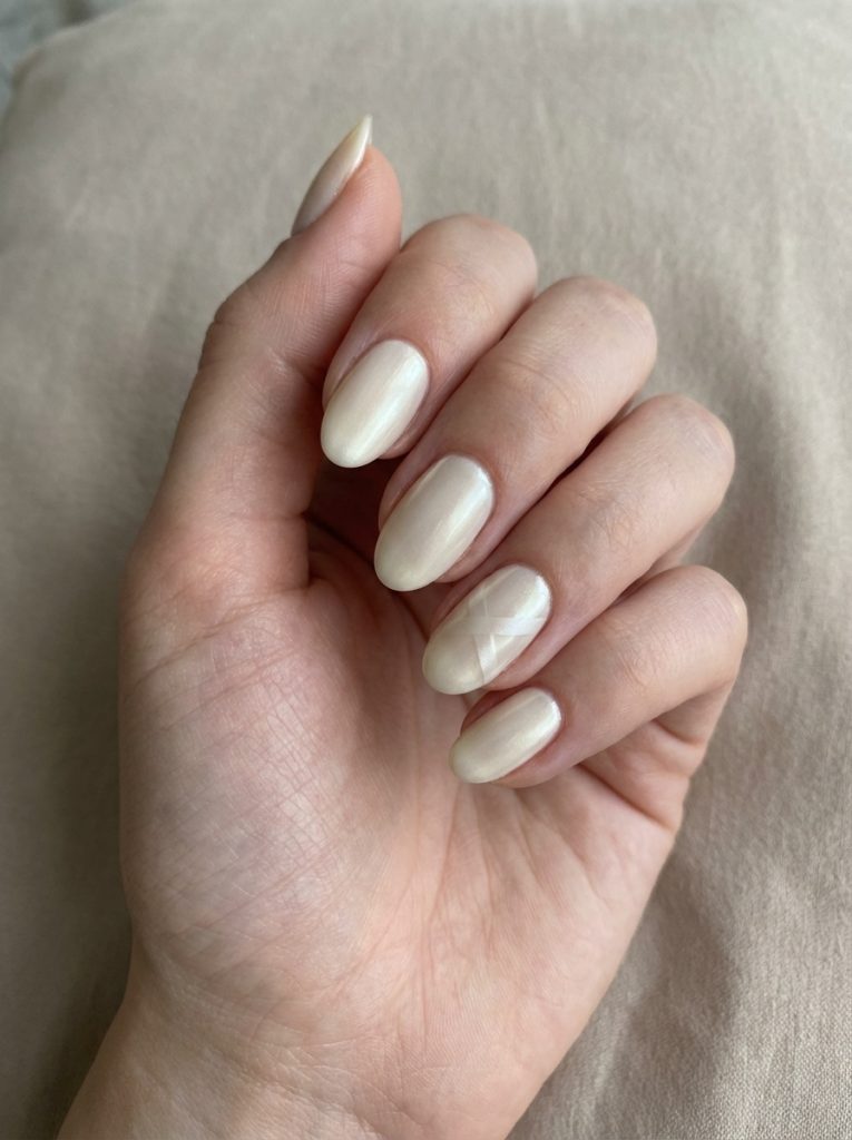 Hand angled inward showing pearl wedding nails in warm alabaster polish with a soft pearly shine and one accent nail featuring thin intersecting line art.
