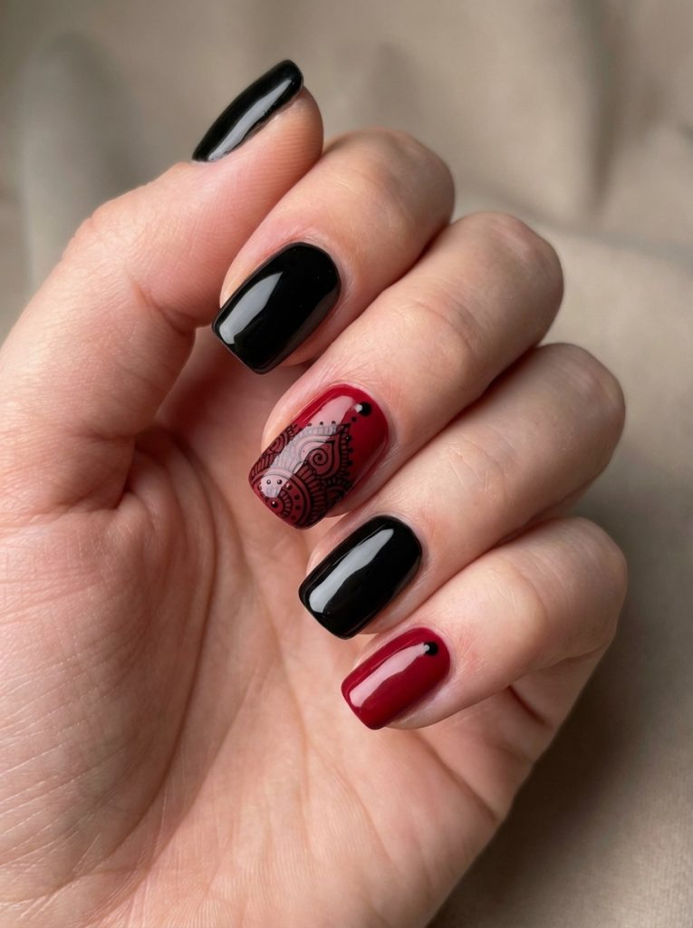 Close-up of a hand showcasing red and black wedding nails with glossy jet black polish, deep crimson red nails, and one accent nail detailed in black lace-like artwork over ruby red.
