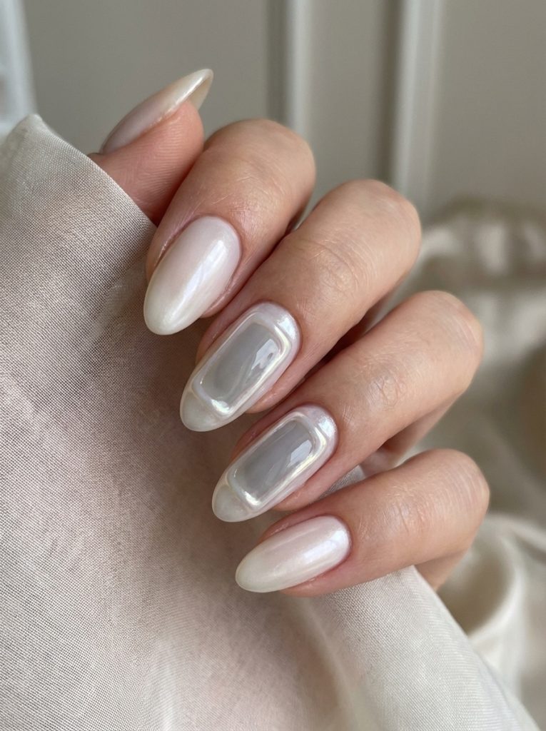Manicured hand with almond-shaped pearl wedding nails in milky white, highlighting two dimensional translucent accent nails with glossy borders.