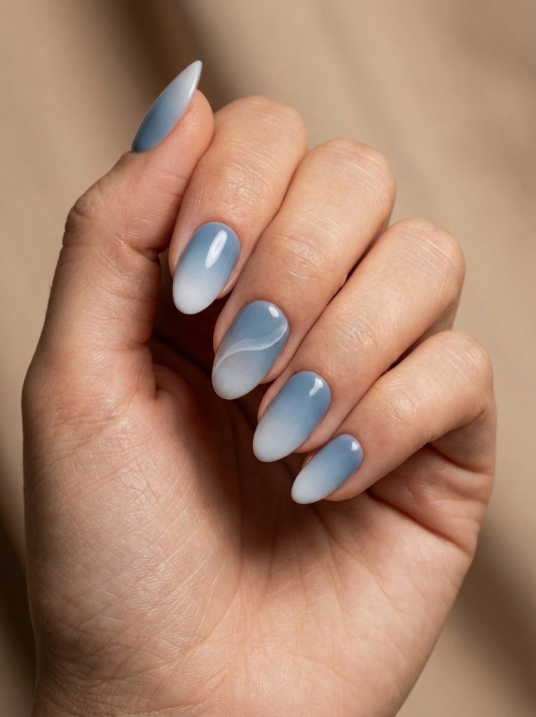 Almond-shaped manicure shown on a gently curled hand, featuring ombre wedding nails in powder blue fading into soft white, with one nail accented by a delicate wave design.