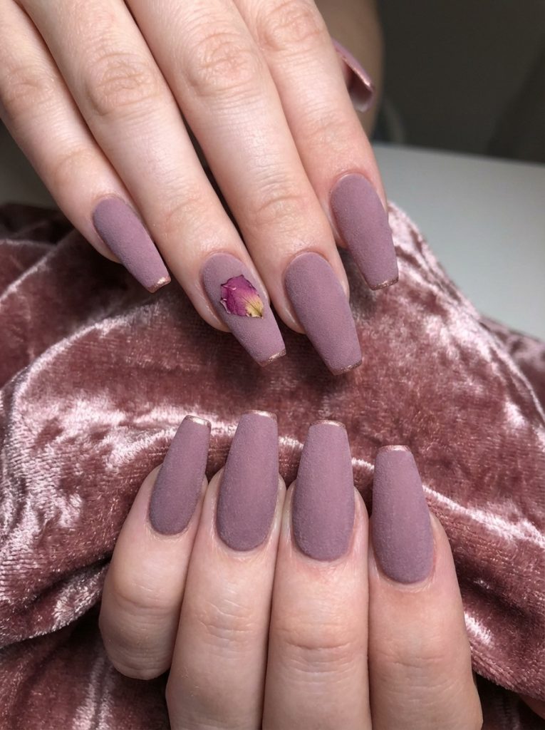 Manicured hands layered over mauve velvet fabric displaying matte wedding nails in smoky mauve with a dried petal design and slim metallic borders.