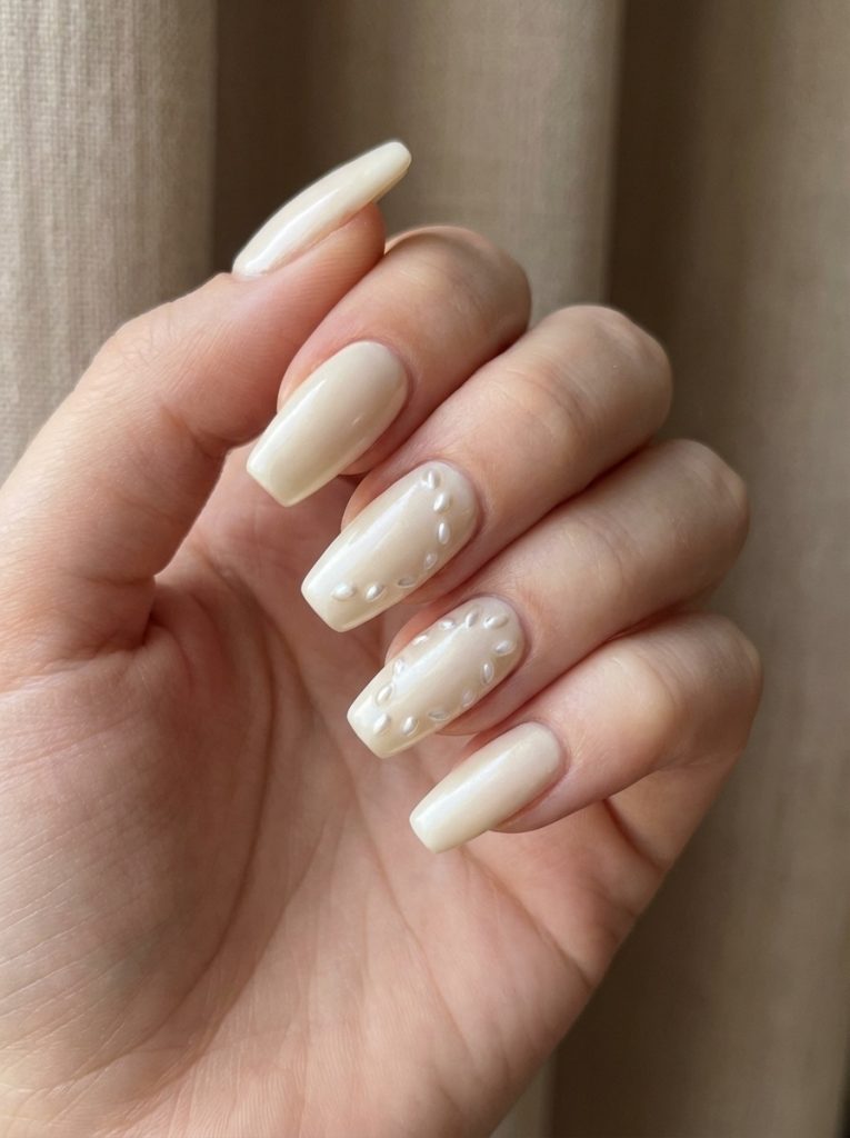 Natural hand angled inward showcasing pearl wedding nails in buttery alabaster polish with textured pearl embellishments arranged across two accent nails.