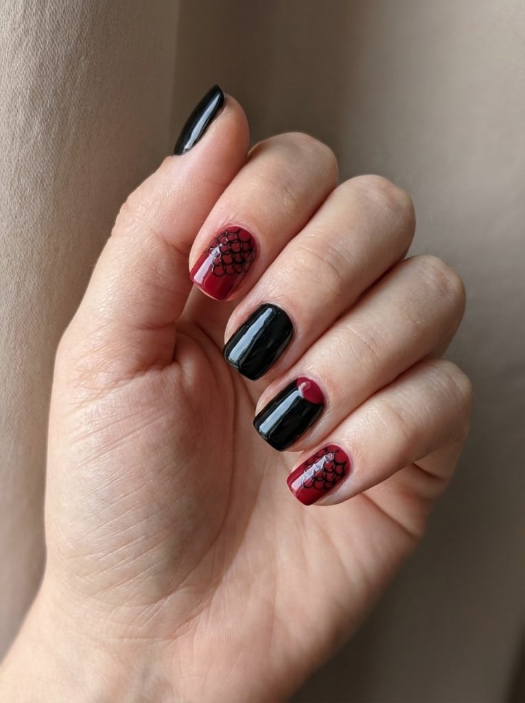 Hand positioned beside a soft curtain displaying red and black wedding nails in glossy black and deep crimson, featuring scale-pattern accents on two nails.