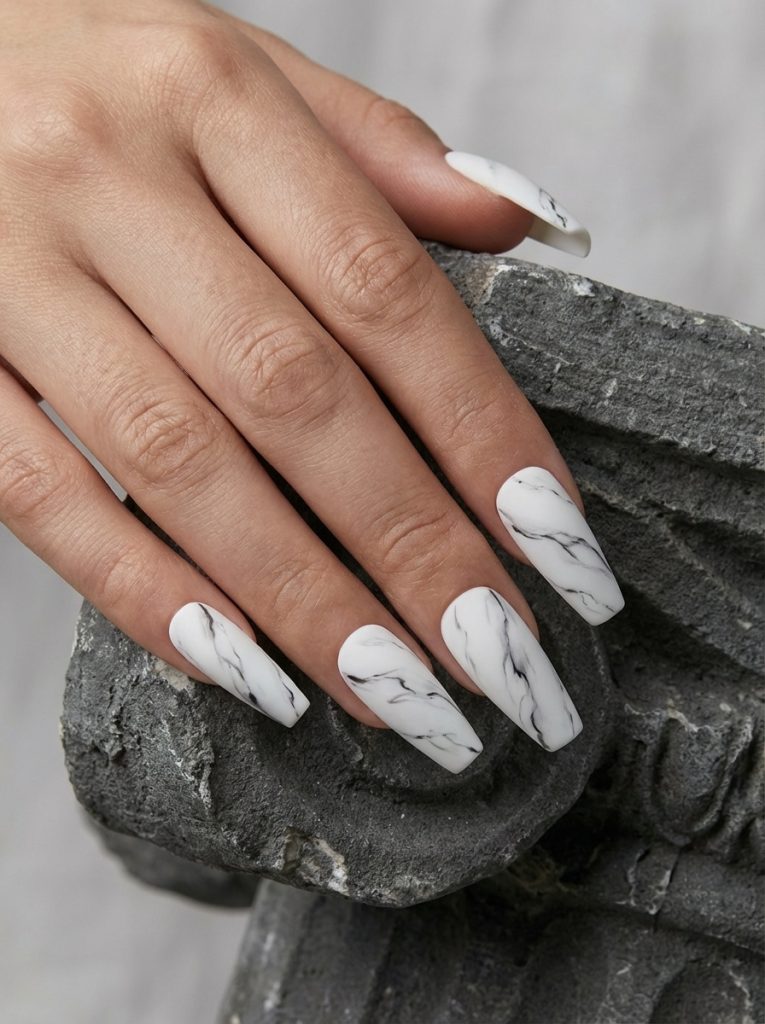 Hand placed over a gray stone ornament showing matte wedding nails in creamy white with thin charcoal marble streaks and a smooth flat finish.