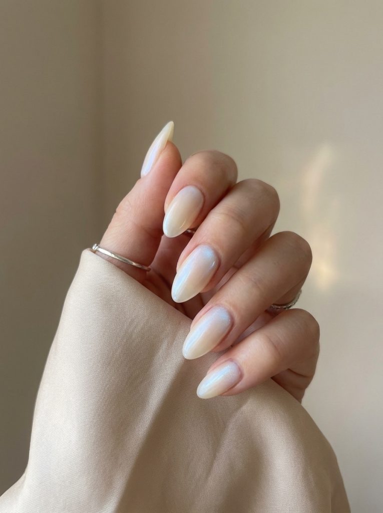 Hand wrapped in beige fabric wearing pearl wedding nails in creamy ivory with subtle blue iridescent reflection and a sleek almond silhouette.