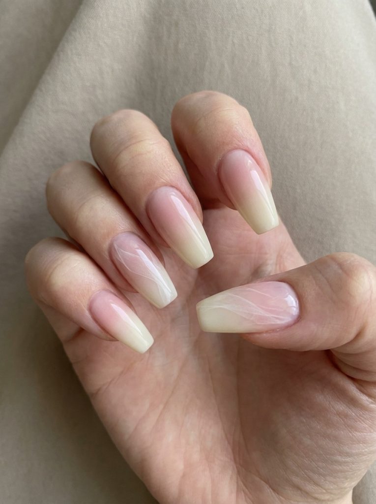 Natural hand pose showcasing long square ombre wedding nails shifting from blush to ivory, featuring delicate white botanical line art across two fingers.