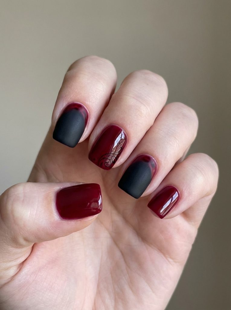 Close-up of a hand against a soft neutral background featuring red and black wedding nails in glossy wine red and matte black, with one nail showcasing a fine scroll design.