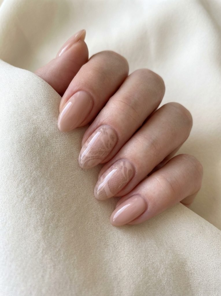 Manicured hand with nude wedding nails in warm beige, featuring accent nails with darker printed design layered subtly beneath the shine.