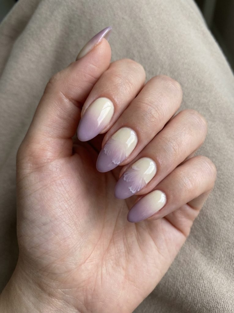 Hand gently curled inward showcasing ombre wedding nails in a cream-to-lilac gradient, highlighted by subtle white petal artwork on the middle fingers.