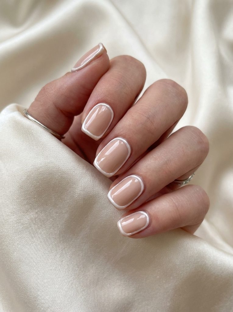 Elegant close-up of hand wearing nude wedding nails in creamy beige with subtle white outline design on glossy short square nails.