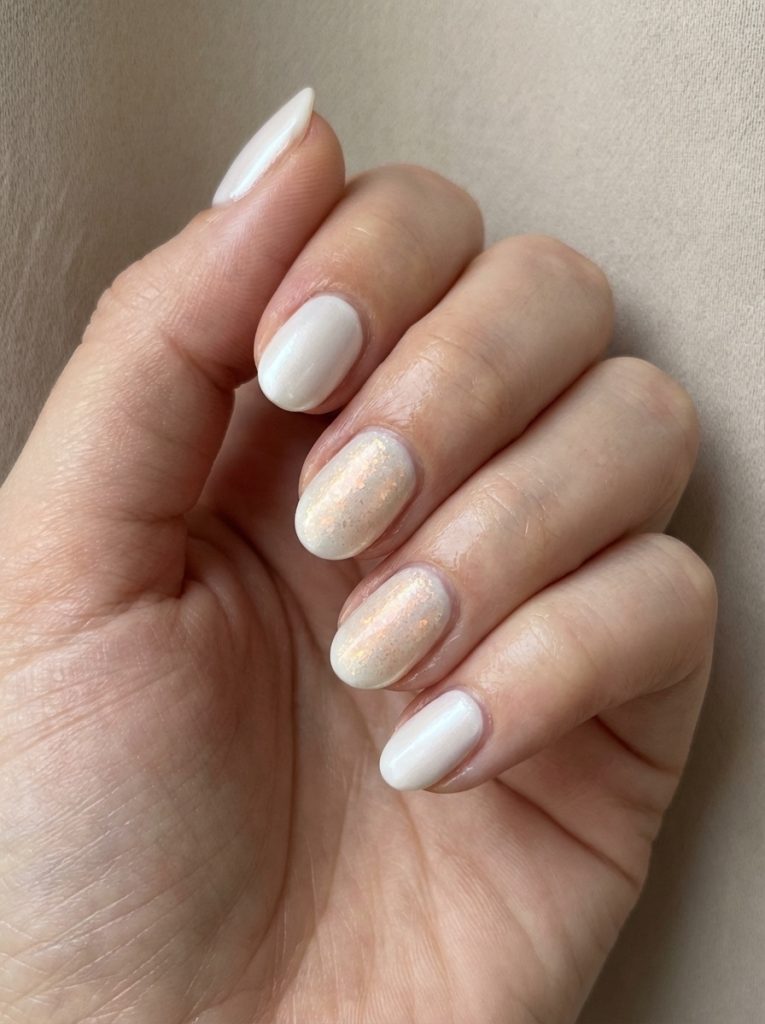 Short natural-shaped pearl wedding nails in creamy ivory shade, accented by two nails coated in translucent champagne glitter polish.
